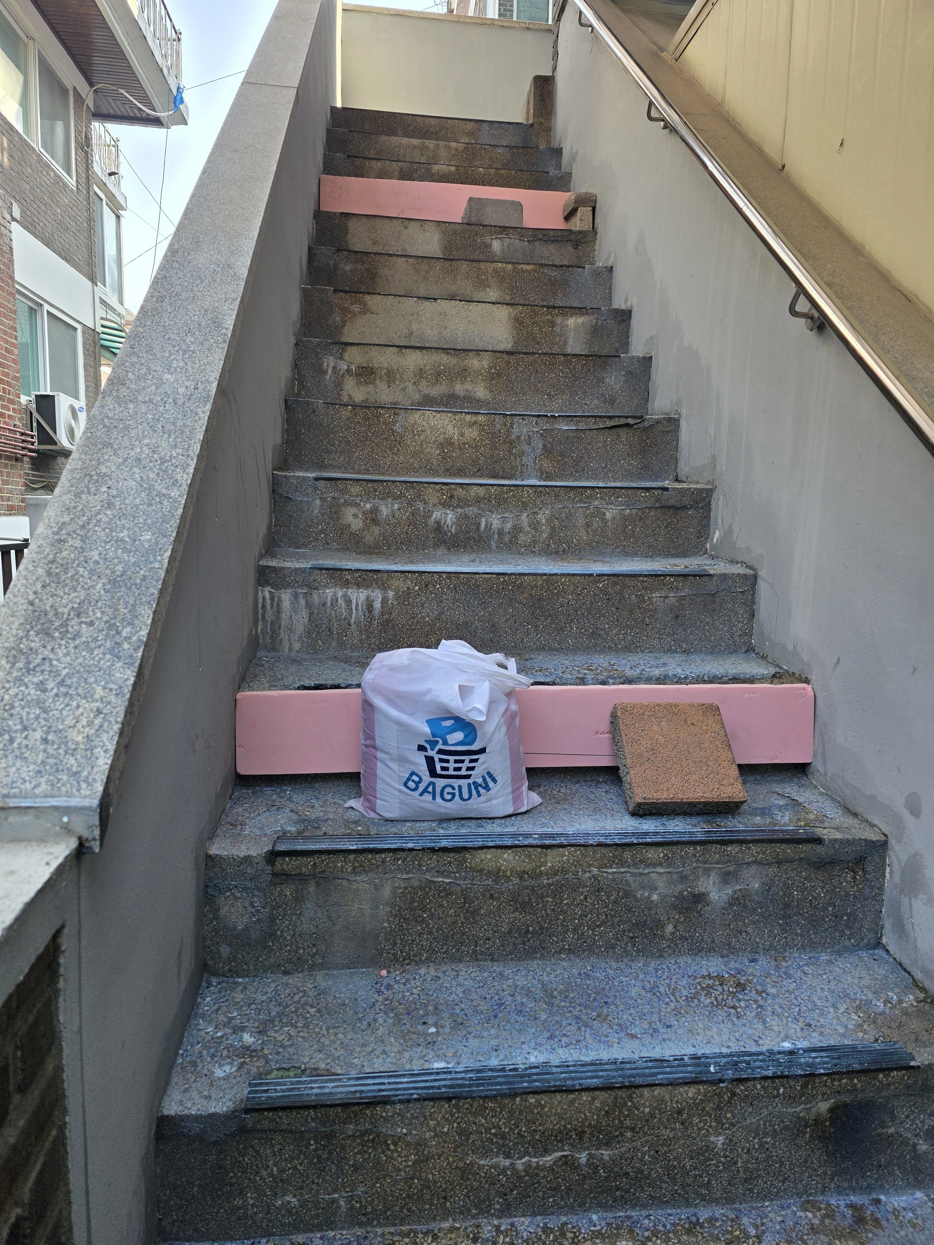 단 위에 분홍 자재와 비닐봉지가 놓인 시공 전 외부 계단