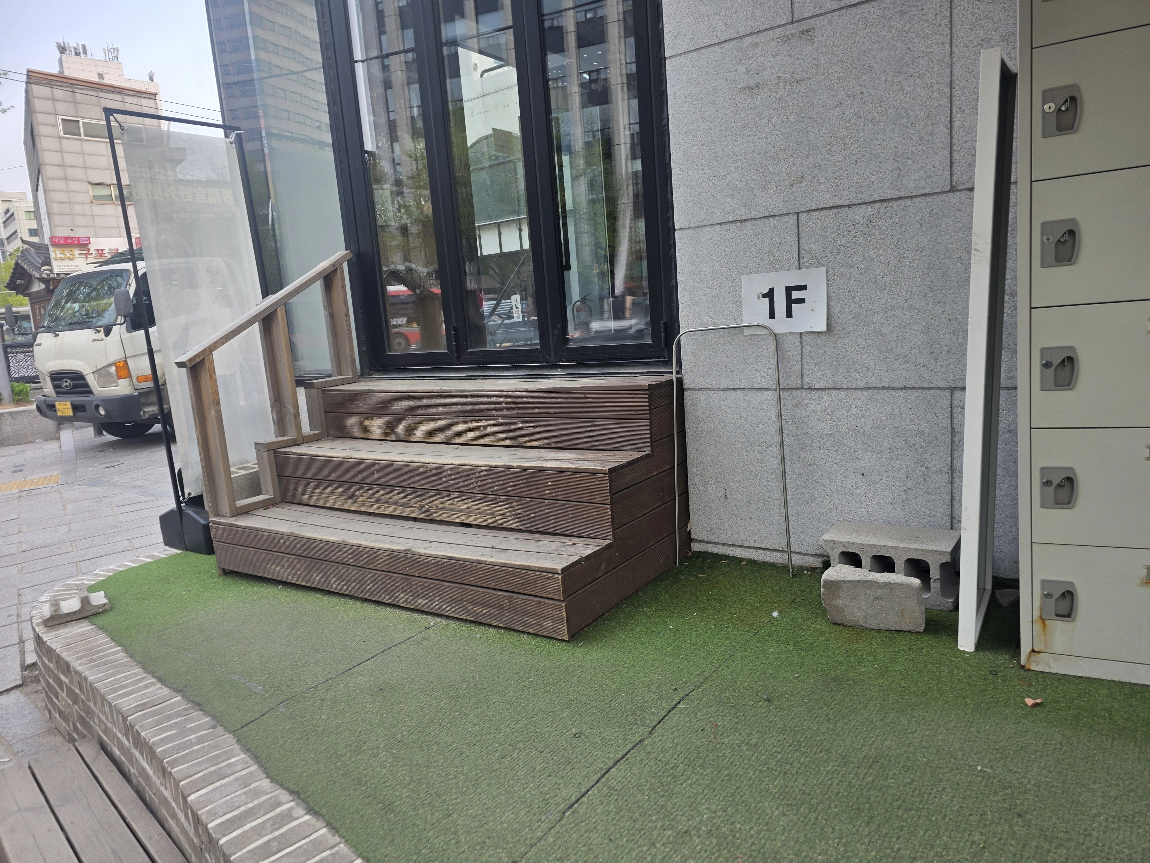 1F 표시가 있는 건물 앞 3단 데크 계단과 난간 기둥